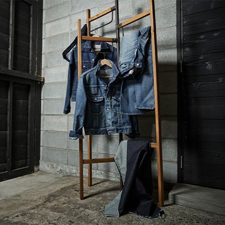 Denim trousers and denim jackets hanging on a wooden clothes rack (Photo)