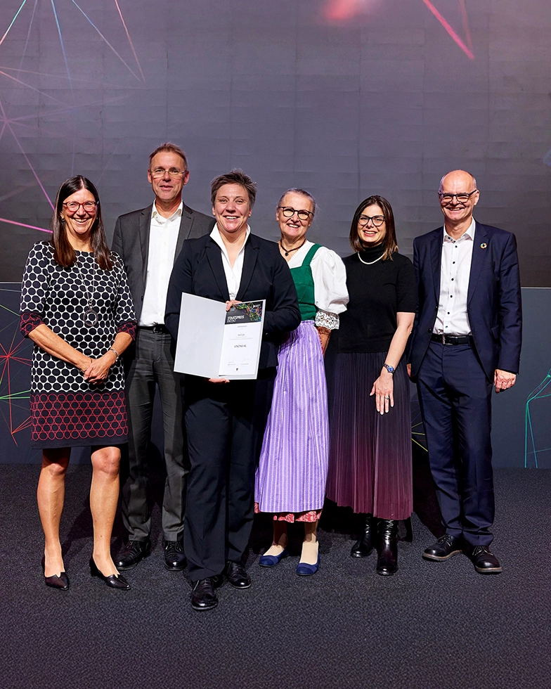 One woman and four men smiling while posing with two awards in front of the camera (Photo)
