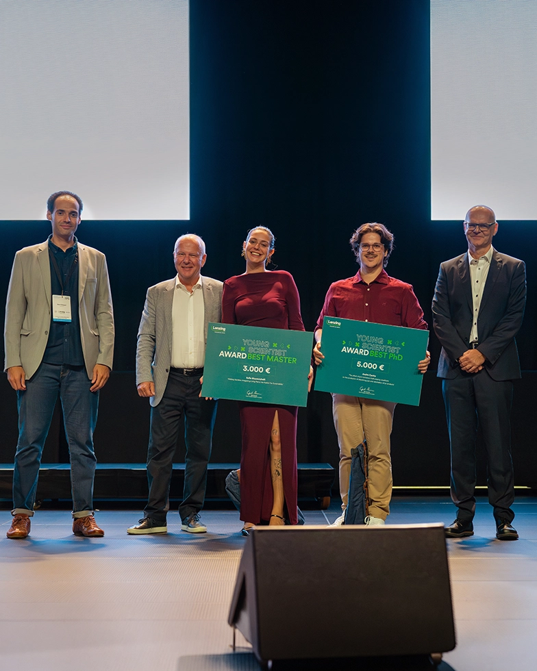 One woman and four men smiling while posing with two awards in front of the camera (Photo)