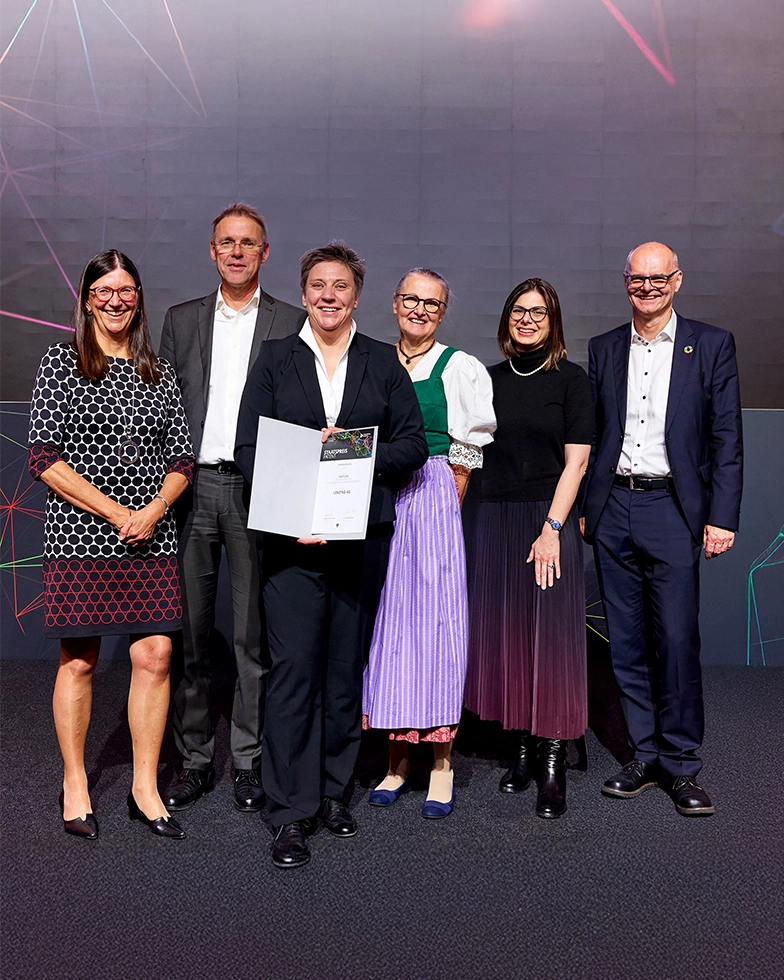 Four women and two men smiling while posing with a certificate in front of the camera (Photo)