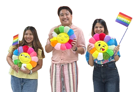 Zwei Frauen und ein Mann halten drei bunte Polster in Blumenform sowie zwei Flaggen in Regenbogenfarben (Foto)